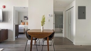 Ein moderner Essbereich mit Holztisch und -stühlen, einer Topfpflanze und Blick in das angrenzende Schlafzimmer.