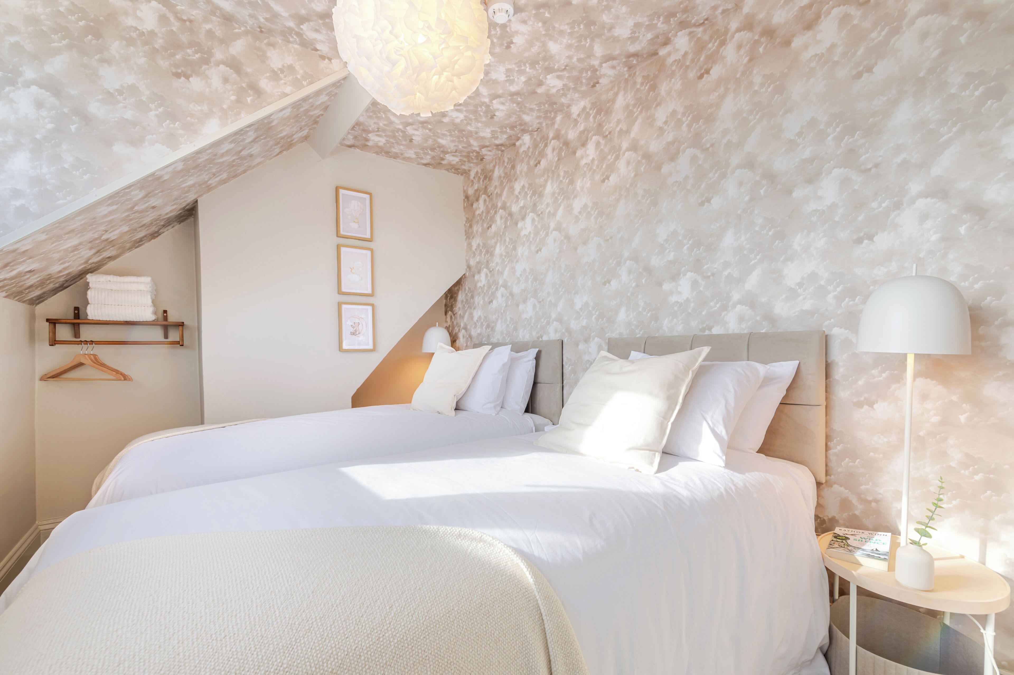 A bedroom with a large bed, a hanging light fixture, a bedside table with a lamp, and a wall-mounted shelf.
