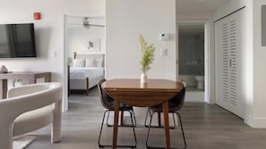 A modern hotel room with a wooden dining table, a TV, a bed, and a shower area. - Landing | Amazing 1BD, Gym (Hialeah)