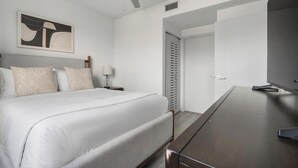 Et hotelværelse med en stor seng, et skrivebord, et fjernsyn og en dør med et ristet vindue.