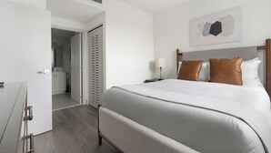 Et hotelværelse med en stor seng, et sengebord med lampe, et klædeskab og et badeværelse, der kan ses gennem en åben dør.