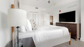 A bedroom with a bed, a bedside table, a lamp, a dresser, a TV, and a door.