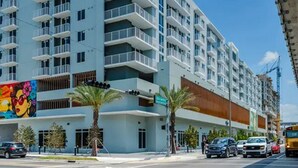 A multi-story hotel with balconies, a street view, and palm trees. - Landing | Chic 1BD, Gym (Hialeah)