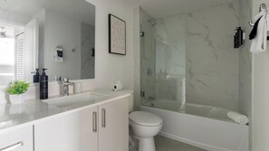 A modern bathroom with a glass-enclosed shower, a white toilet, and a sink with a mirror. - Landing | Stylish 1BD, Gym (Hialeah)