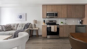 Eine moderne Küche mit Holzschränken, einer eingebauten Mikrowelle, einem Herd und einem Geschirrspüler. Ein kleiner Tisch steht dort mit einer Lampe und einer Pflanze.