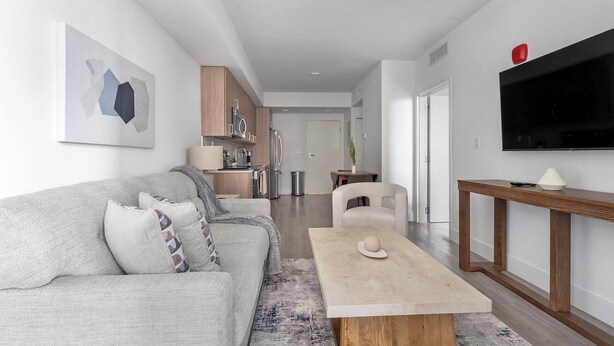 A modern living room with a grey sofa, a coffee table, and a TV mounted on the wall. - Landing | Stylish 1BD, Gym (Hialeah)