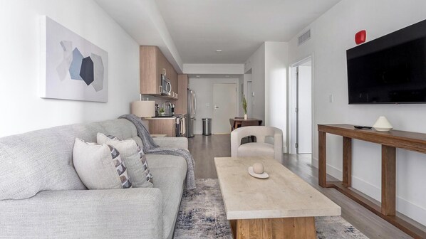 A modern living room with a grey sofa, a coffee table, and a TV mounted on the wall. - Landing | Stylish 1BD, Gym (Hialeah)