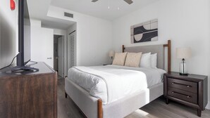 A bedroom with a bed, bedside table, lamp, and a TV on a stand. - Landing | Stylish 1BD, Gym (Hialeah)