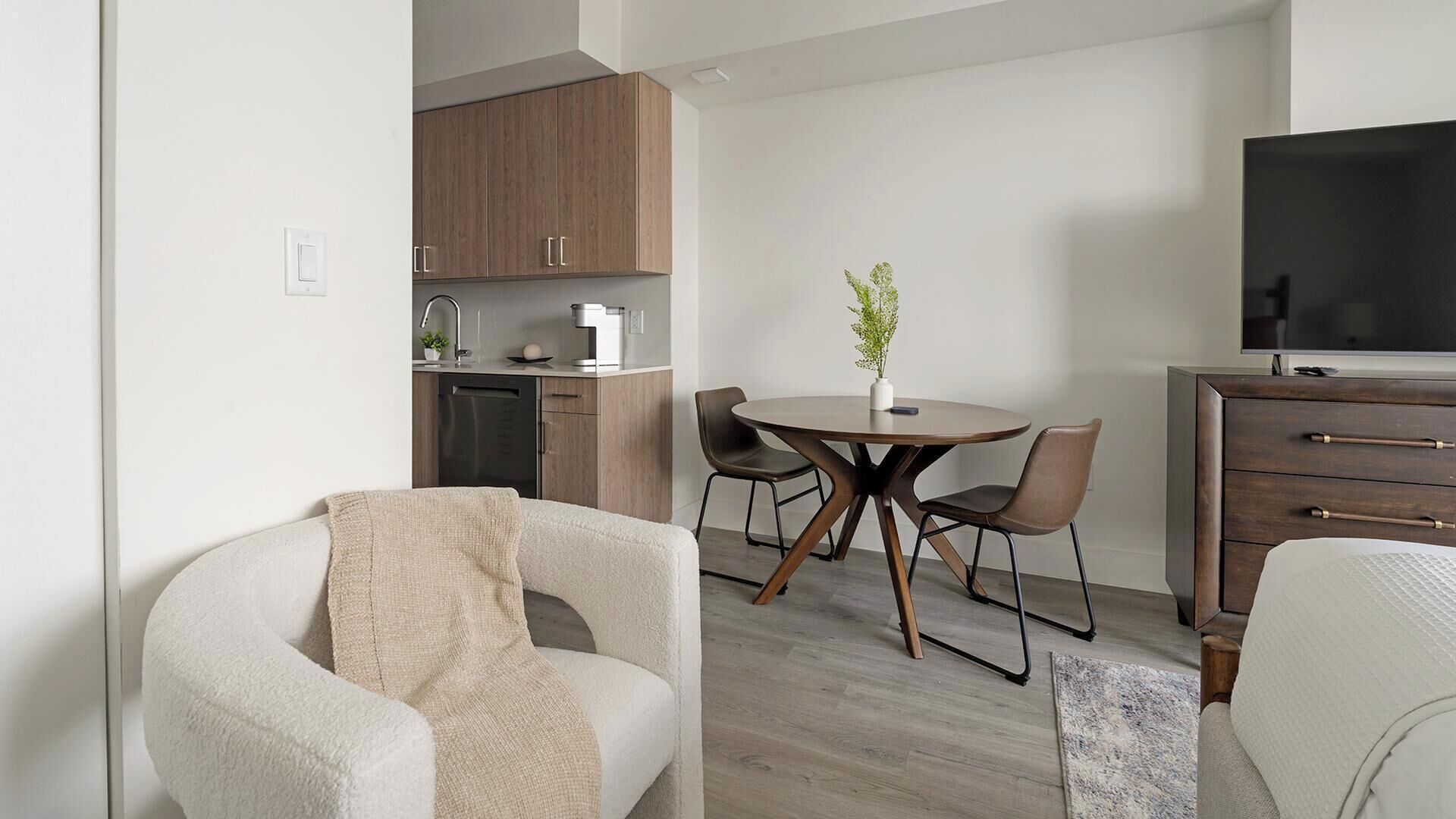 Een moderne woonkamer met een bank, een eettafel met stoelen, een televisie en een keuken met houten kasten en apparatuur.
