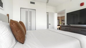 A bedroom with a bed, a dresser, a television, and a door leading to a kitchen. - Landing | Stunning 1BD, Gym (Hialeah)