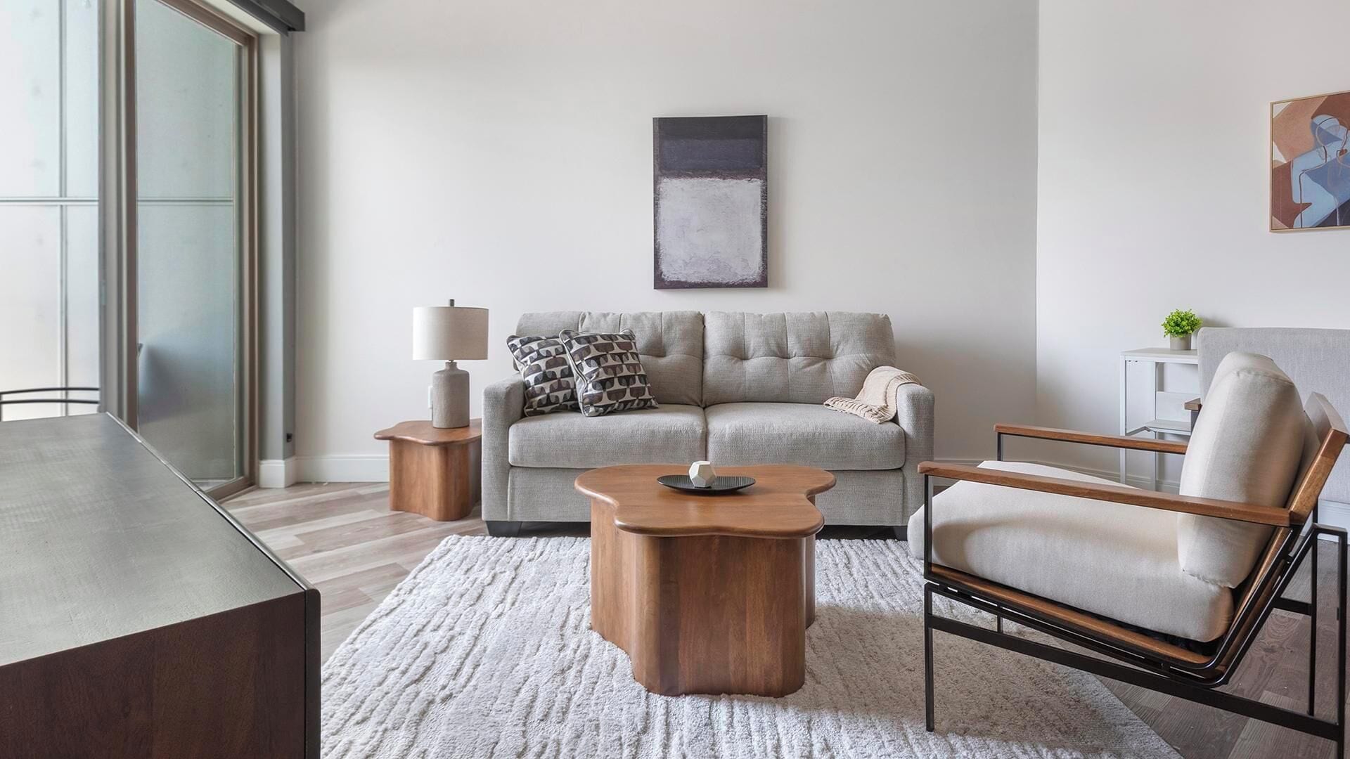 A modern living room with a sofa, coffee table, and armchair, a side table, and a painting on the wall.