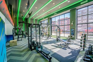 A gym with various exercise equipment, large windows, and a chevron-patterned floor. - Landing | Stunning 1BD, Gym, Yoga Studio (St. Louis)