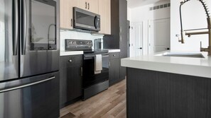A modern kitchen with stainless steel appliances, a microwave, and a built-in oven. - Landing | Chic 2BD, Yoga Studio, Gym (St. Louis)