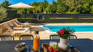 Zona piscina con sedie a sdraio, un tavolo con bevande e frutta, e vista sulla piscina.