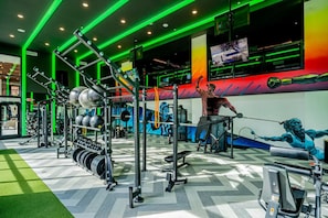 Une salle de sport équipée de matériel d’exercice, d’un écran de télévision et ornée d’une fresque murale.