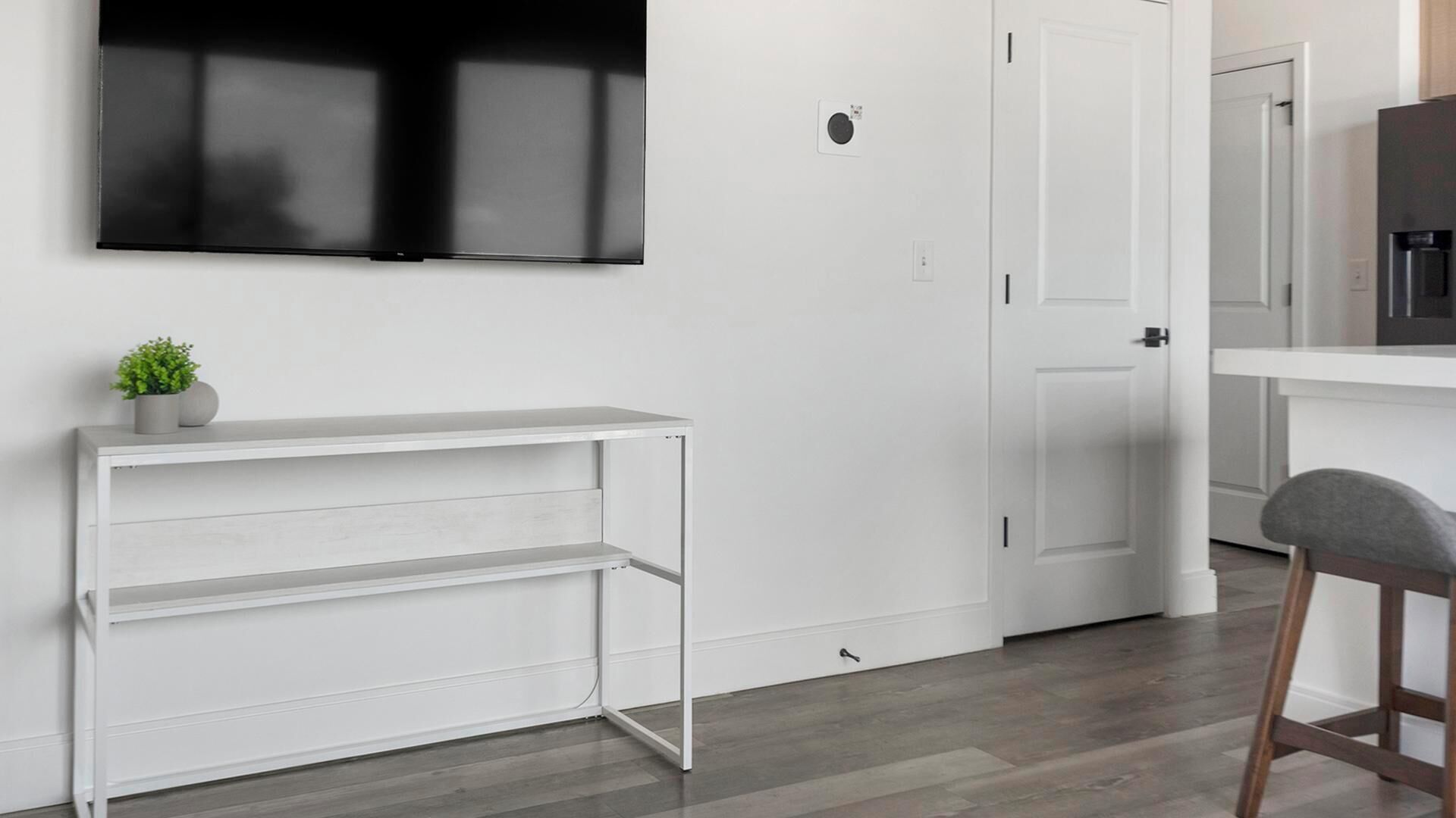 Una cucina moderna con un piano di lavoro bianco, una televisione montata a parete e una porta che dà su un'altra stanza.