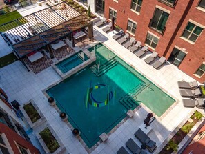 An aerial view of a rooftop pool with a slide, surrounded by lounge chairs and a wooden deck. - Landing | Stunning 1BD, Gym, Yoga Studio (St. Louis)