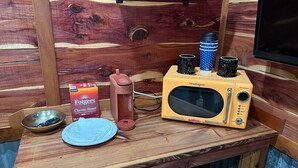 A kitchenette with a microwave, coffee maker, and a box of Folgers Classic Roast coffee. - Whoa-Man Ultra Cozy Aggieland  Cabin (North Zulch)