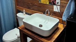 A bathroom with a wooden wall, a white sink, a toilet, and a shower curtain. - Whoa-Man Ultra Cozy Aggieland  Cabin (North Zulch)