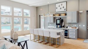 A modern kitchen with a bar area, large windows, and a view of a swimming pool. - Landing | Modern 2BD, Clubhouse (Pensacola)