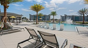 A poolside area with lounge chairs, a pool, and a building in the background. - Landing | Spectacular 2BD in St. Cloud (Kissimmee)