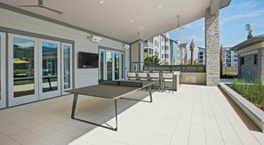 Un patio al aire libre con mesa de ping pong, asientos y una pantalla de televisión.