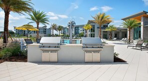 An outdoor grill area with two gas grills, a pool, and lounge chairs. - Landing | Spectacular 2BD in St. Cloud (Kissimmee)