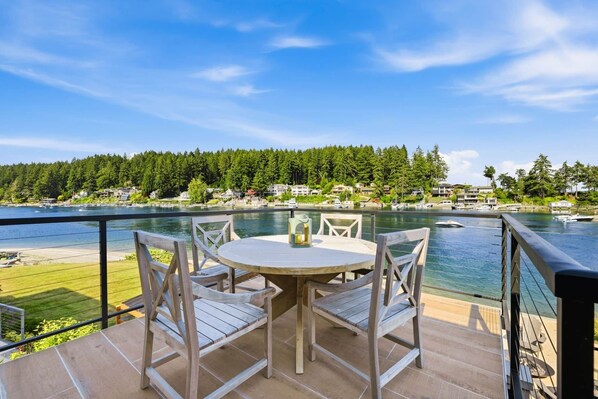 Une terrasse en bois avec une table ronde et des chaises, d’où l’on a vue sur une étendue d’eau, avec des bateaux et des maisons en arrière-plan.