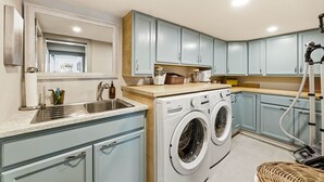 A compact kitchen with a built-in washing machine, a sink, and light blue cabinets. - Luxury Waterfront Home walk to Downtown Gig Harbor (Gig Harbor)