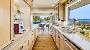 A modern kitchen with a view of the sea, wooden cabinets, and a dining area with a round table. - Luxury Waterfront Home walk to Downtown Gig Harbor (Gig Harbor)