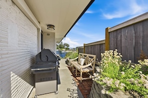 An outdoor patio with a barbecue grill, a wooden bench, and a stone planter with flowers. - Luxury Waterfront Home walk to Downtown Gig Harbor (Gig Harbor)