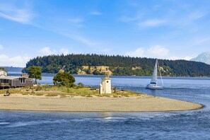 A coastal scene with a lighthouse, a sailboat, and a house by the water. - Luxury Waterfront Home walk to Downtown Gig Harbor (Gig Harbor)