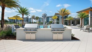 Ein Grillbereich im Freien mit zwei Gasgrills, einem Pool und Liegestühlen.