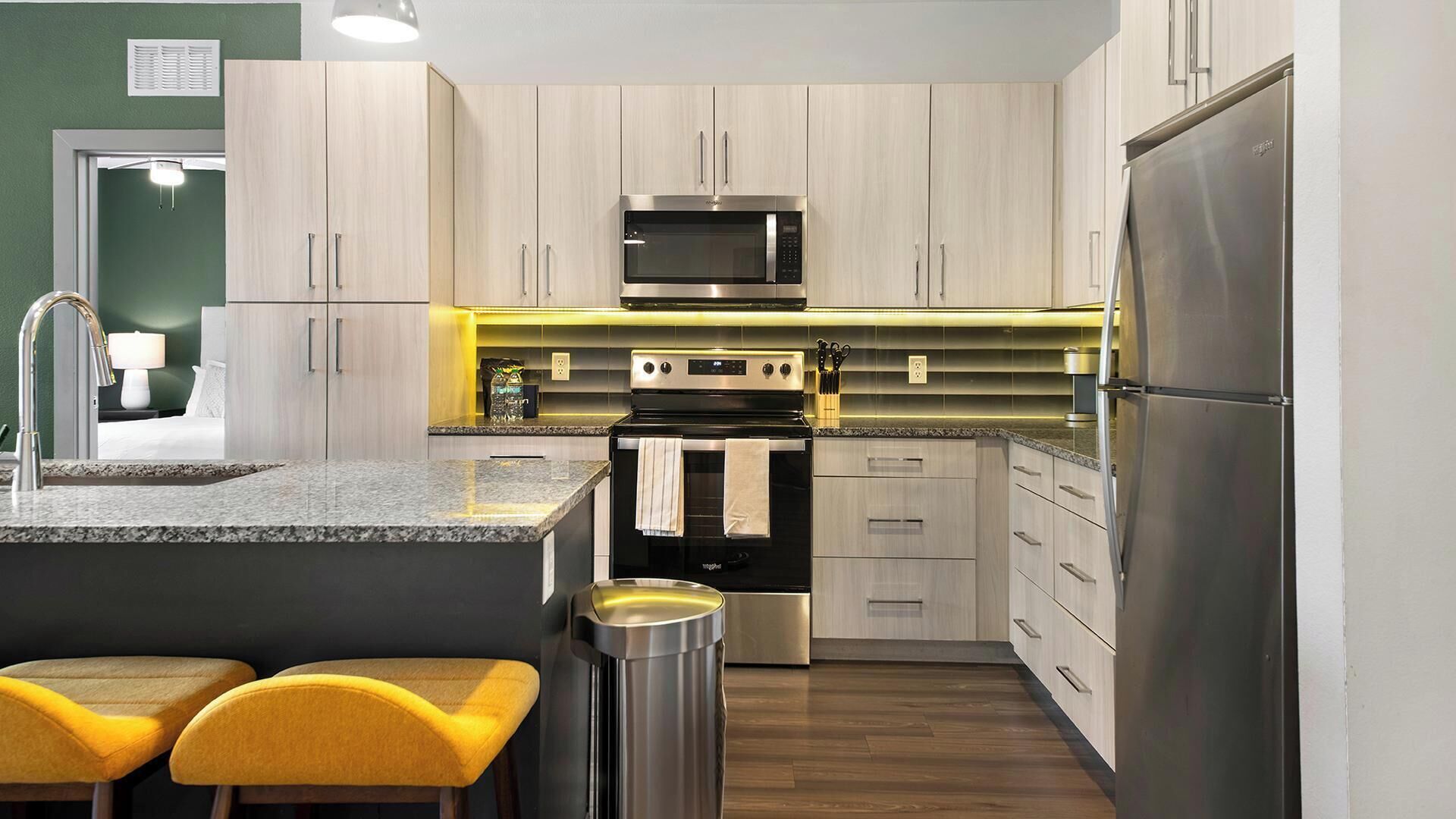 Una cocina moderna con una isla central, electrodomésticos de acero inoxidable y taburetes amarillos.