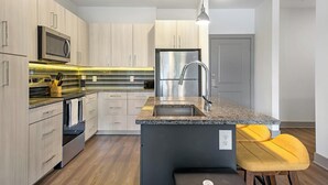 Cocina moderna con electrodomésticos de acero inoxidable, encimera de granito y una isla integrada con taburetes de bar.