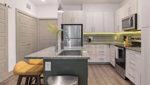 A modern kitchen with a granite countertop, stainless steel appliances, and wooden cabinetry. - Landing | Chic 1BD in St. Cloud (Kissimmee)