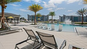 A poolside area with lounge chairs, a pool, and a building in the background. - Landing | Chic 1BD in St. Cloud (Kissimmee)