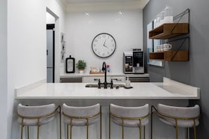 Eine moderne Küche mit einer zentralen Kochinsel, Barhocker, einer Kaffeemaschine und einer Wanduhr.