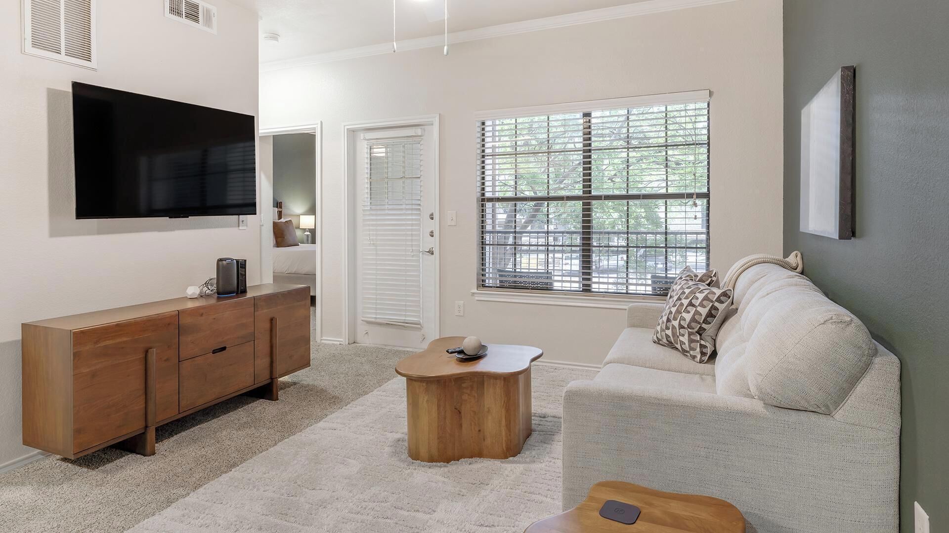 A living room with a TV, wooden furniture, a sofa, and a window with blinds.