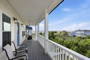 Eine überdachte Veranda mit weißen Geländern, einem Schaukelstuhl und Blick auf ein blaues Haus im Hintergrund.