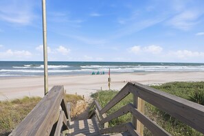 A wooden boardwalk leading to a beach with waves in the background.
