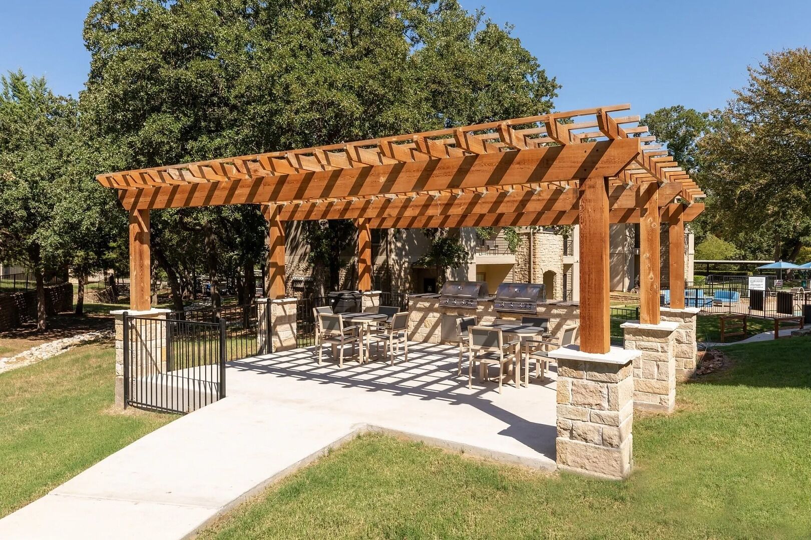 Un patio al aire libre con pérgola, pilares de piedra y zona de barbacoa.