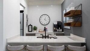 Eine moderne Küche mit einer zentralen Kochinsel, Barhocker, einer Kaffeemaschine und einer Wanduhr.