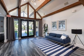 A spacious room with a large window, a blue sofa, a floor lamp, and a striped rug. - Landing | Stunning 2BD, Gym (Lewisville)