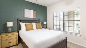A bedroom with a bed, two bedside tables, a nightstand, a window with blinds, and a wall-mounted artwork. - Landing | Incredible 2BD, Gym (Lewisville)