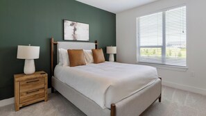 A bedroom with a bed, two bedside tables, a nightstand, a window with blinds, and a wall-mounted artwork. - Landing | Spectacular 2BD in Frisco - Fields (Frisco)