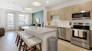 A modern kitchen with a central island, stainless steel appliances, and light wood cabinetry. - Landing | Modern 1BD, Rooftop Lounge, Gym (Frisco)