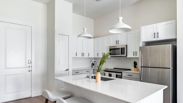 A modern kitchen with white cabinetry, stainless steel appliances, and a central island with bar stools. - Landing | Modern 1BD, Rooftop Lounge, Gym (Frisco)
