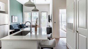 A modern kitchen with a central island, a dining area with a sofa, and a living space with a TV. - Landing | Modern 1BD, Rooftop Lounge, Gym (Frisco)