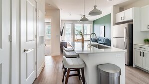 A modern kitchen with a central island, bar stools, a sink, and a refrigerator. - Landing | Amazing 1BD, Gym, Rooftop Lounge (Frisco)